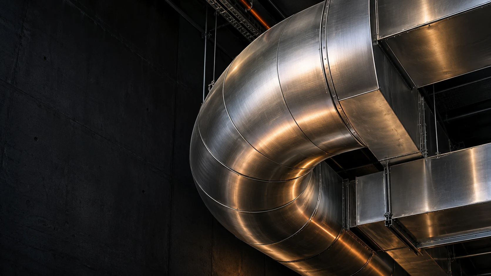 Conceptual architectural photograph of a sculptural silver ventilation duct in a dark building interior.